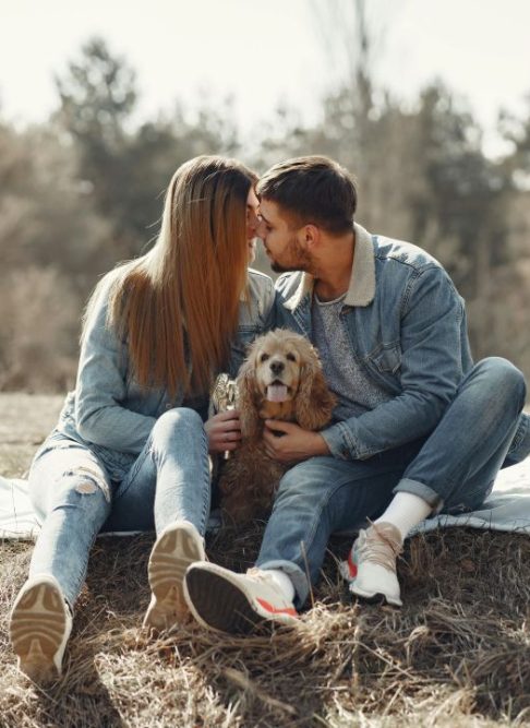 couple_en_exterieur_assis_sur_l_herbe_avec_leur_chien_dans_les_bras_au_centre_de_la_photo